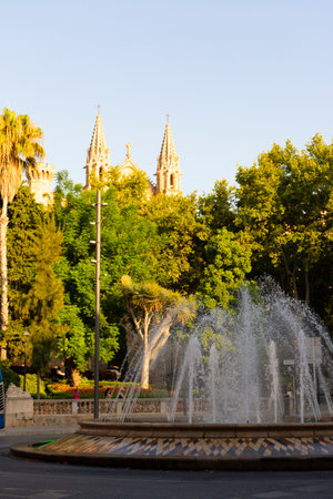 Palma, Mallorca, Balearic Islands, Spain. July 21, 2022 - Fountain in the roundabout of the Plaza de la Reina, or Queen square with the towers of the Palma Cathedral in the background, at sunsetのeditorial素材