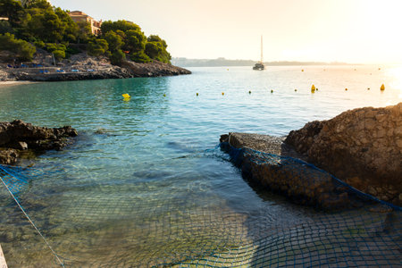 Catamaran anchored off the rocky coast of Ses Illetes, with the city of Palma in the background, at sunriseの写真素材