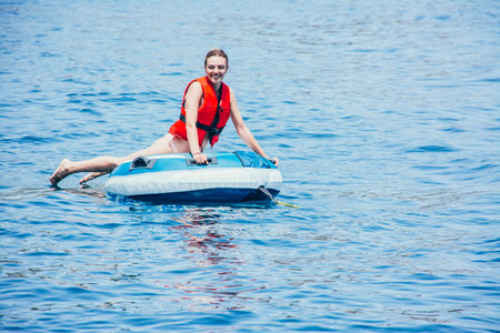Smiling young woman enjoying in the sea on an inflatable donut, looking at the cameraの写真素材