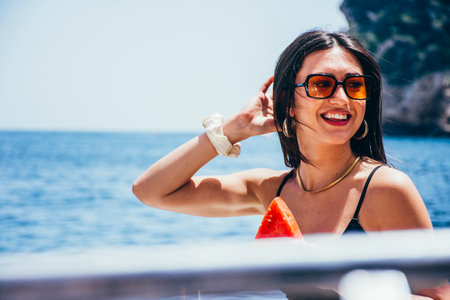 Young woman in sunglasses eating watermelon on a boat sailing the sea in summerの写真素材
