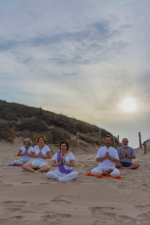 Group of men and women practicing yoga on the sand at the beach. Padmasana or lotus asanaの写真素材