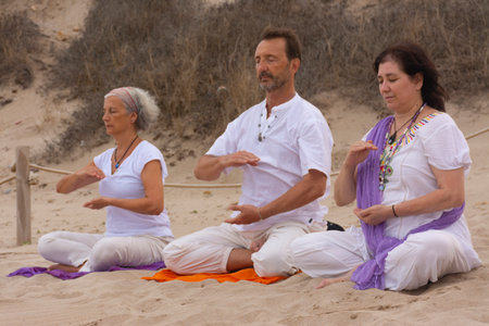 Group of men and women practicing kundalini yoga on the sand at the beach.の写真素材