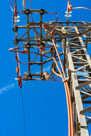 Top of a power line tower with cables and network details, seen from just below, with blue sky. Vertical imageの写真素材