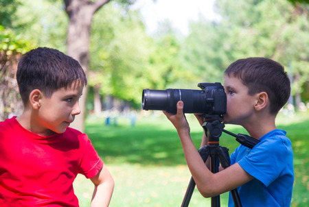 Two boys have fun with a camera outdoors. Two brothers enjoy taking pictures of each other in a park. Sunny September morning in Almaty, Kazakhstan.の写真素材