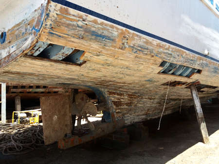 Wooden fishing boat under repair at the dock on the shores of the Red Sea in the open air. Iron ship propeller with rusty blades. The cut planks of the ship's hull and the skeleton is visible.の写真素材