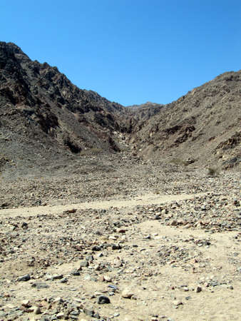 Rocky soil near gray mountain with blue skyの写真素材