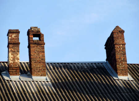 Brick chimneys on the slate roof of an old house. Red with smoke stack with damage and blue skyの写真素材