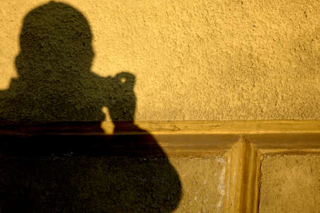 Correct. Silhouette shadow of a photographer guy on the wall with textured plaster and gold paint in recessesの写真素材