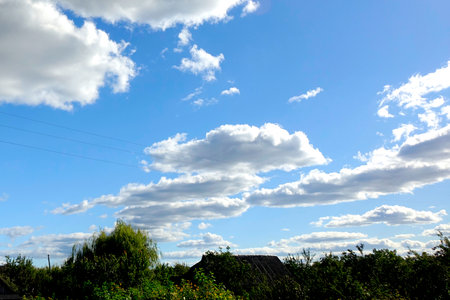 Fluffy white clouds float across a bright blue sky, casting shadows over the lush greenery of the peaceful countryside.の写真素材