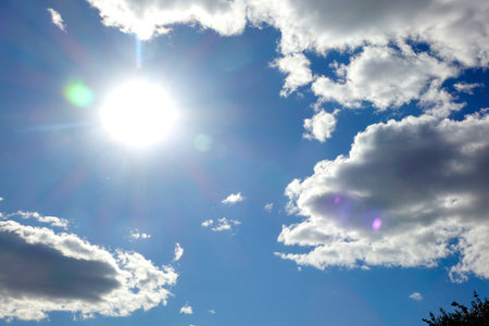 The sun shines brightly in a vivid blue sky, scattered with fluffy white clouds, creating a serene and uplifting atmosphere.の写真素材