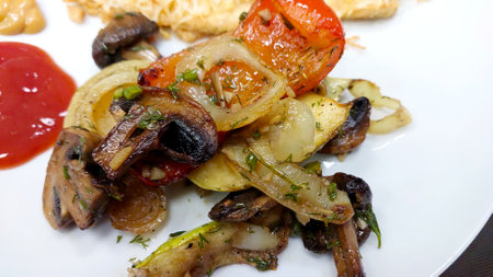 A colorful assortment of grilled vegetables and mushrooms is plated alongside a serving of ketchup for added flavor.の写真素材