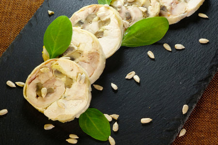 Tender meat roll slices arranged on a black ceramic board, garnished with fresh spinach leaves and scattered sunflower seeds.の写真素材