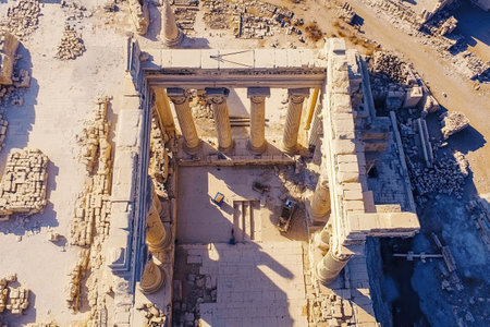 The remnants of an ancient temple are visible, showcasing towering columns and scattered stone blocks under bright daylight. The site appears abandoned, highlighting historical significance.の素材