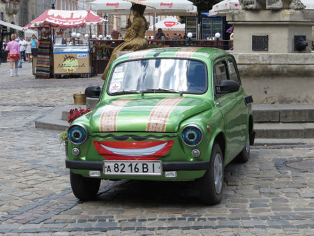 Lviv, Ukraine - July 20, 2013 A cheerful ZAZ-965 Zaporozhets vintage green car adorned with a playful smile sits parked in a bustling town square. People stroll by, enjoying the vibrant atmosphere under the warm sun.のeditorial素材