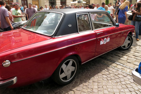 Lviv, Ukraine - June 14, 2015 Classic red automobile VOLVO 162 DE LUXE in a busy town square filled with festival activities under a bright sky. Lively interactions and festive decorationsのeditorial素材