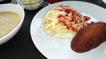 Savory spaghetti topped with tangy sauce pairs perfectly with a succulent cutlet, served alongside a warm broth and fresh salad for a delightful meal.の写真素材
