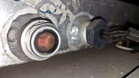 Close examination of an oil sump plug shows intricate details in a workshop setting. Surrounding tools hint at ongoing maintenance work on the vehicle systems.の写真素材