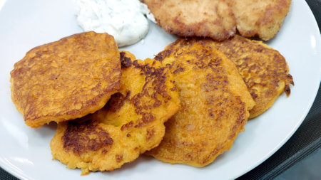 Delicious potato pancakes are plated with a dollop of tangy sauce and crispy sides, inviting diners to experience comforting flavors and textures in a relaxed atmosphere.の写真素材
