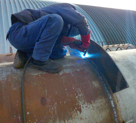 A skilled welder concentrates on welding a large pipe, using protective gear while sparks fly from...