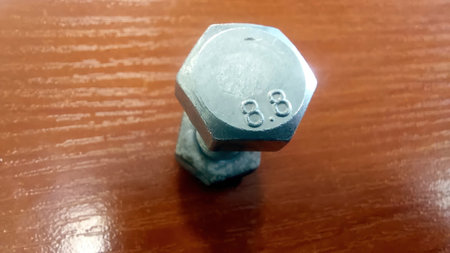 Close-up of a metallic bolt with an 8.8 grade marking, positioned on a wooden table, showing its hexagonal shape and shiny surface.の写真素材