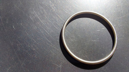 A round spring rests on a flat, smooth surface illuminated by sunlight, casting intricate shadows and highlighting its metallic texture and shape.の写真素材