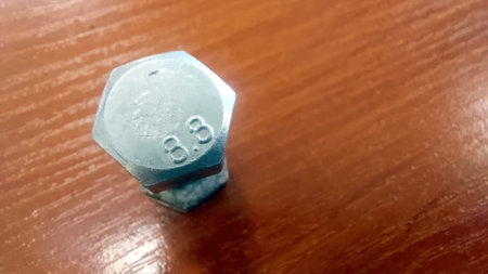A metallic hexagonal bolt is positioned on a polished wooden table, showing its shiny surface and engraved 8.8 markings while reflecting the surroundings.の写真素材