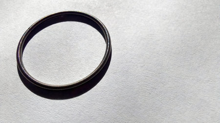 A round spring is placed on a smooth white paper surface, illuminated by soft light that creates a subtle shadow, emphasizing its circular shape and texture.の写真素材