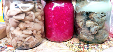 Various glass jars filled with canned mushrooms, pickled vegetables, and a sweet preserve sit on a kitchen counter, showing home canning skills and vibrant colors.の写真素材