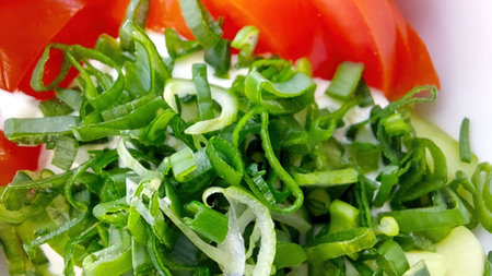A colorful salad features ripe tomatoes, chopped onions, and fresh green herbs, ideal for a nutritious dish that is refreshing and flavorful.の写真素材