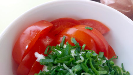 A vibrant salad bowl features sliced red tomatoes and finely chopped onions, topped with fresh green herbs. Perfect for a light, healthy meal at any time of the day.の写真素材