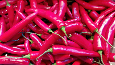 Bright red hot pepper pods fill the display at a local market, showing their glossy texture and vibrant colors under the midday sun, inviting shoppers to explore.の写真素材
