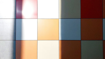 Brightly colored tiles cover the floor, showing a pattern of orange, white, and red tiles. Shadows cast by natural light create dynamic shapes and lines.の写真素材