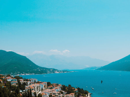 Herceg Novi offers a stunning view of the Bay of Kotor, featuring charming coastal homes, boats, and a backdrop of majestic mountains under a clear blue sky.の写真素材