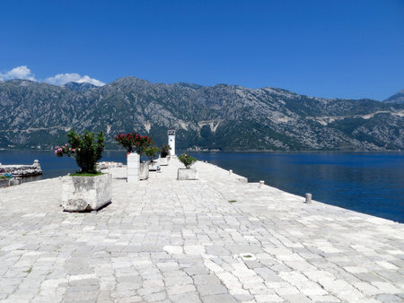 Visitors enjoy the beautiful path on Our Lady of the Rocks island, surrounded by mountains and clear blue water. The serene atmosphere enhances the experience for all.の写真素材