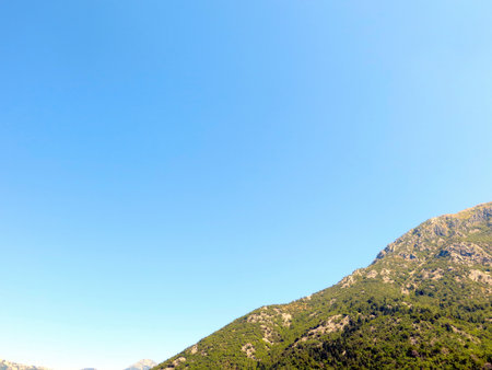 Clear blue skies enhance the stunning landscape of Montenegros Bay of Kotor Riviera, highlighting the lush green mountains and serene waters that attract visitors year-round.の写真素材