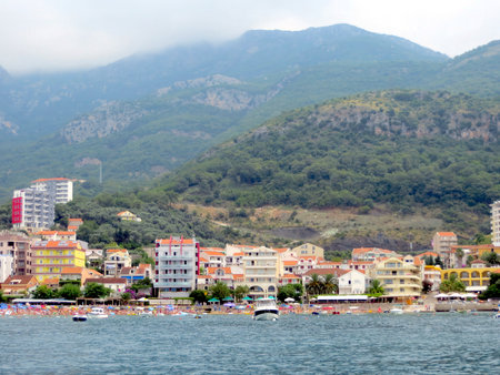 The stunning Budva coastline vibrant features hotels, sandy beaches, and a marina filled with boats, all set against majestic mountains on a cloudy day.の写真素材