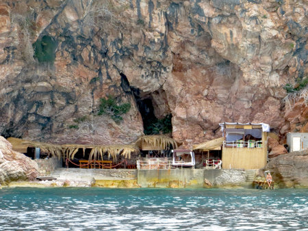Visitors bask in the sun on a rocky beach in Budva, Montenegro, with a charming beach bar nestled against rugged cliffs and vibrant blue water.の写真素材