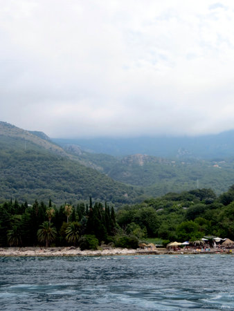 Visitors enjoy the stunning view of Budvas beach, where clear waters meet lush green hills under a cloudy sky, providing a tranquil atmosphere for relaxation.の写真素材