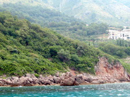 This stunning view showcases the rocky coastline of Montenegro along the Adriatic Sea, surrounded by vibrant greenery and distant structures under a calm sky.の写真素材