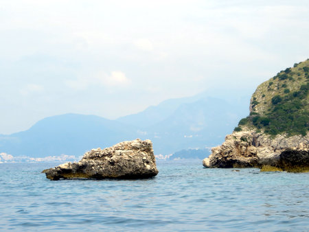 Rocky formations rise from the calm waters of the Adriatic Sea, showing the natural beauty of Montenegro's coastline on an overcast day.の写真素材