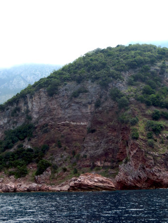 Montenegros rocky coast features striking cliffs and dense greenery, creating a serene landscape along the Adriatic Sea. The calm waters reflect the dramatic terrain.の写真素材