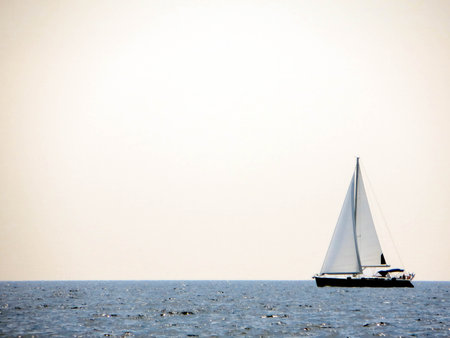 A sail yacht moves gracefully across the tranquil sea, its white sails catching the breeze under a clear sky.の写真素材
