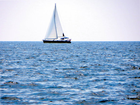 A sleek sail yacht navigates the smooth sea, surrounded by sparkling water under a vast, clear sky. Gentle waves create a peaceful atmosphere on a sunny day.の写真素材