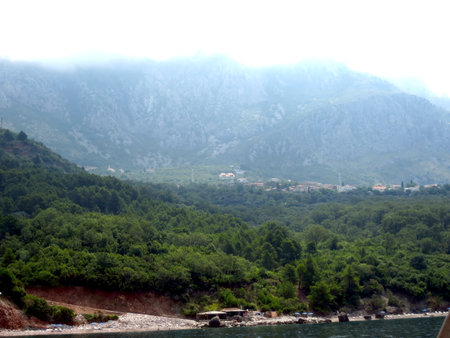 The rocky coastline of Montenegro features lush greenery and majestic mountains under a cloudy sky. A serene atmosphere surrounds the Adriatic Sea as waves gently lap the shore.の写真素材