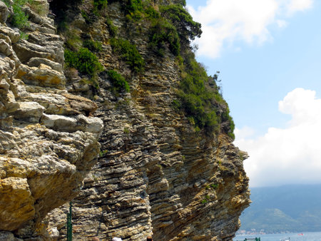 Majestic rock cliffs rise dramatically from the shoreline in Montenegro, surrounded by lush greenery and clear blue skies. Visitors enjoy the natural beauty and serenity.の写真素材