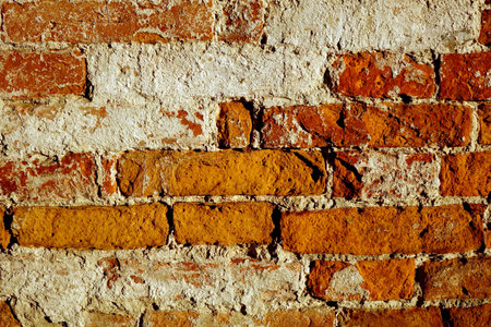 Red brick wall displays rough texture with colors of orange and red. It stands in an urban area...