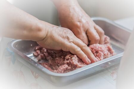 Hands knead minced on white background for concept design. Female put meat in a meat grinderの写真素材