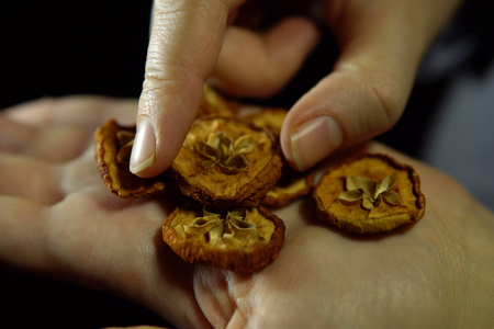 Close-up of a human hand with a handful of round pieces of dry apple in the palm of a hand against a black background, unrecognizable person.の写真素材