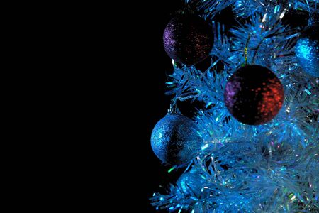 Close-up of shiny white and red balls hanging on a silver artificial Christmas tree in the rays of blue lighting on a black background, selective focus and place for text .の写真素材