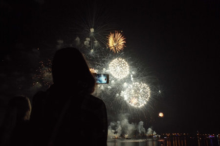 Silhouette of a girl with a smartphone on the background of bright colorful fireworks in the black...